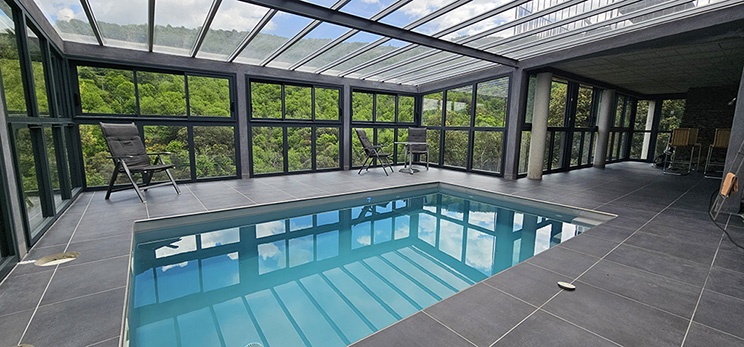 Piscine intérieure sous verrière avec couverture de piscine intégrée, extension moderne issue d’une rénovation de maison en pierre dans les Cévennes